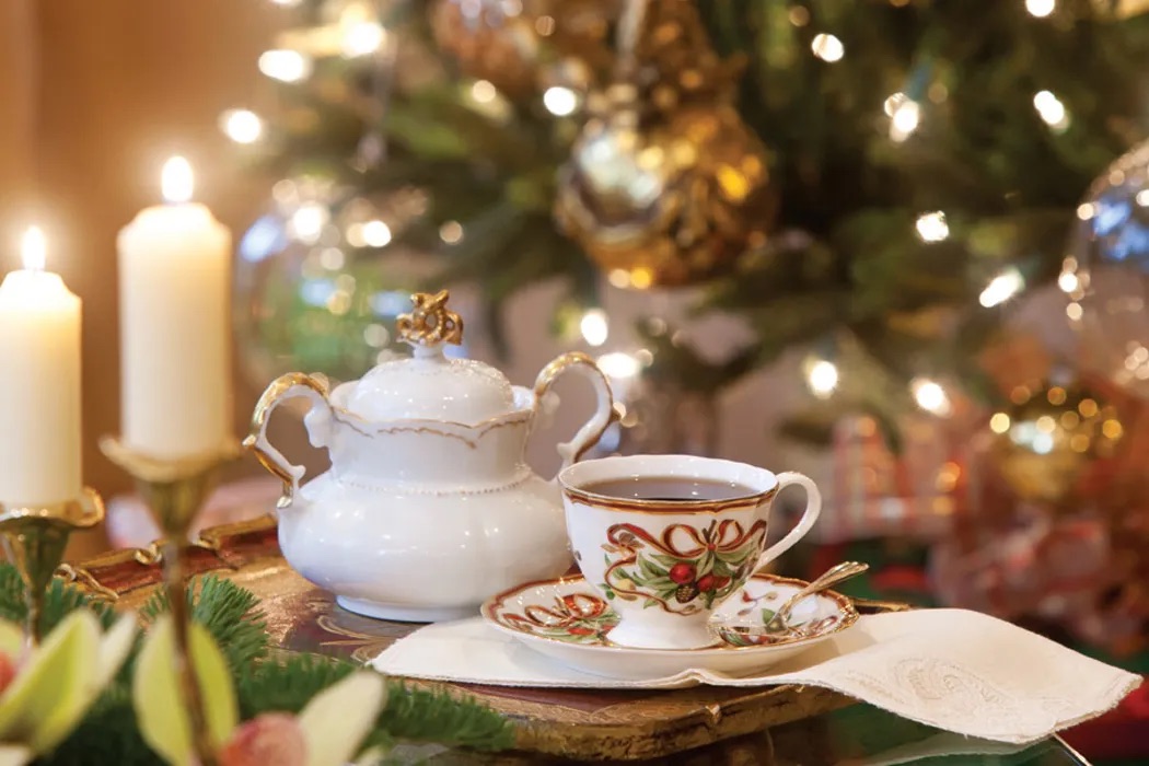 A cup of tea and a teapot in front of a Christmas tree.