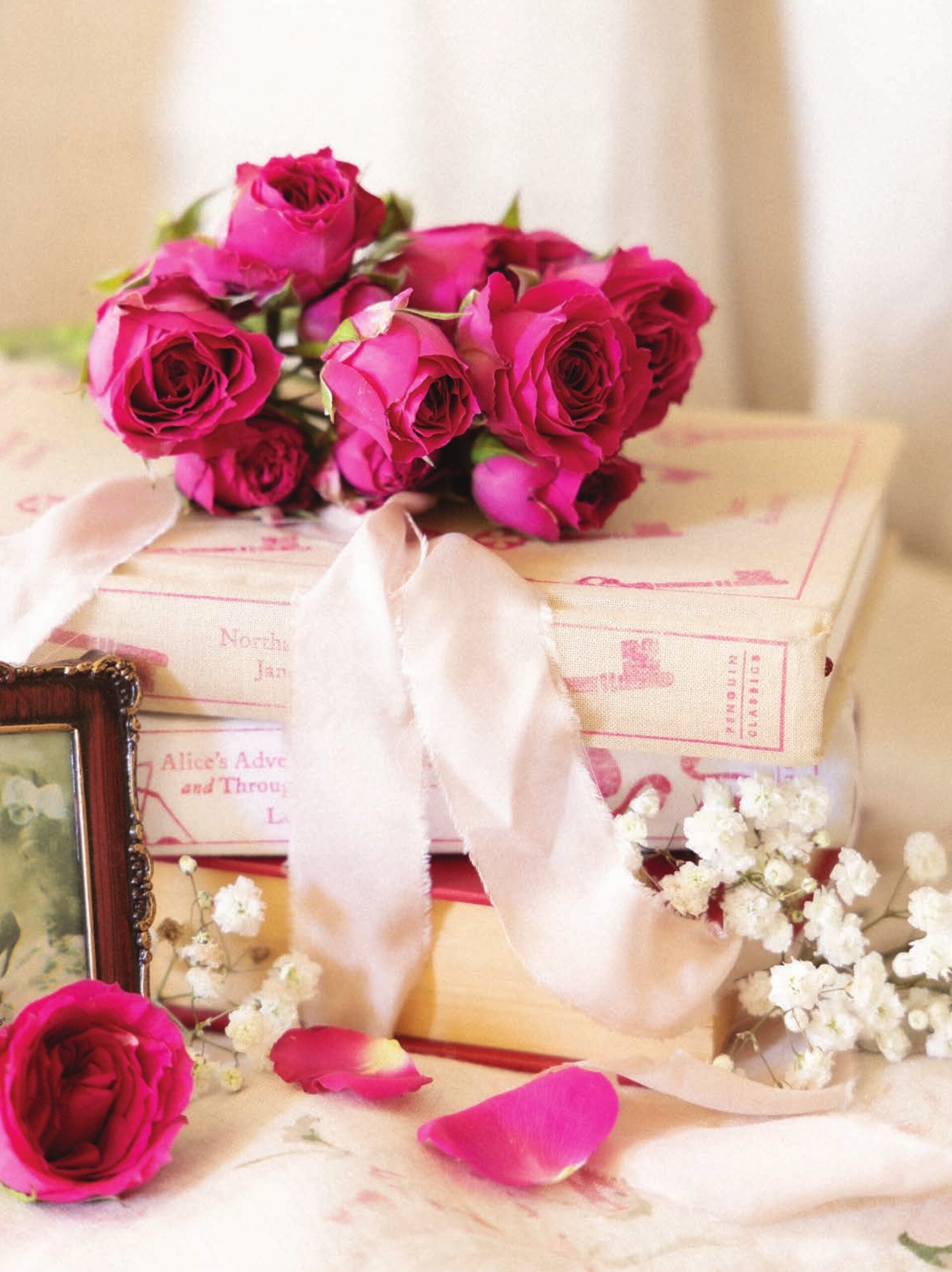 A stack of pink books topped with a bouquet of roses.