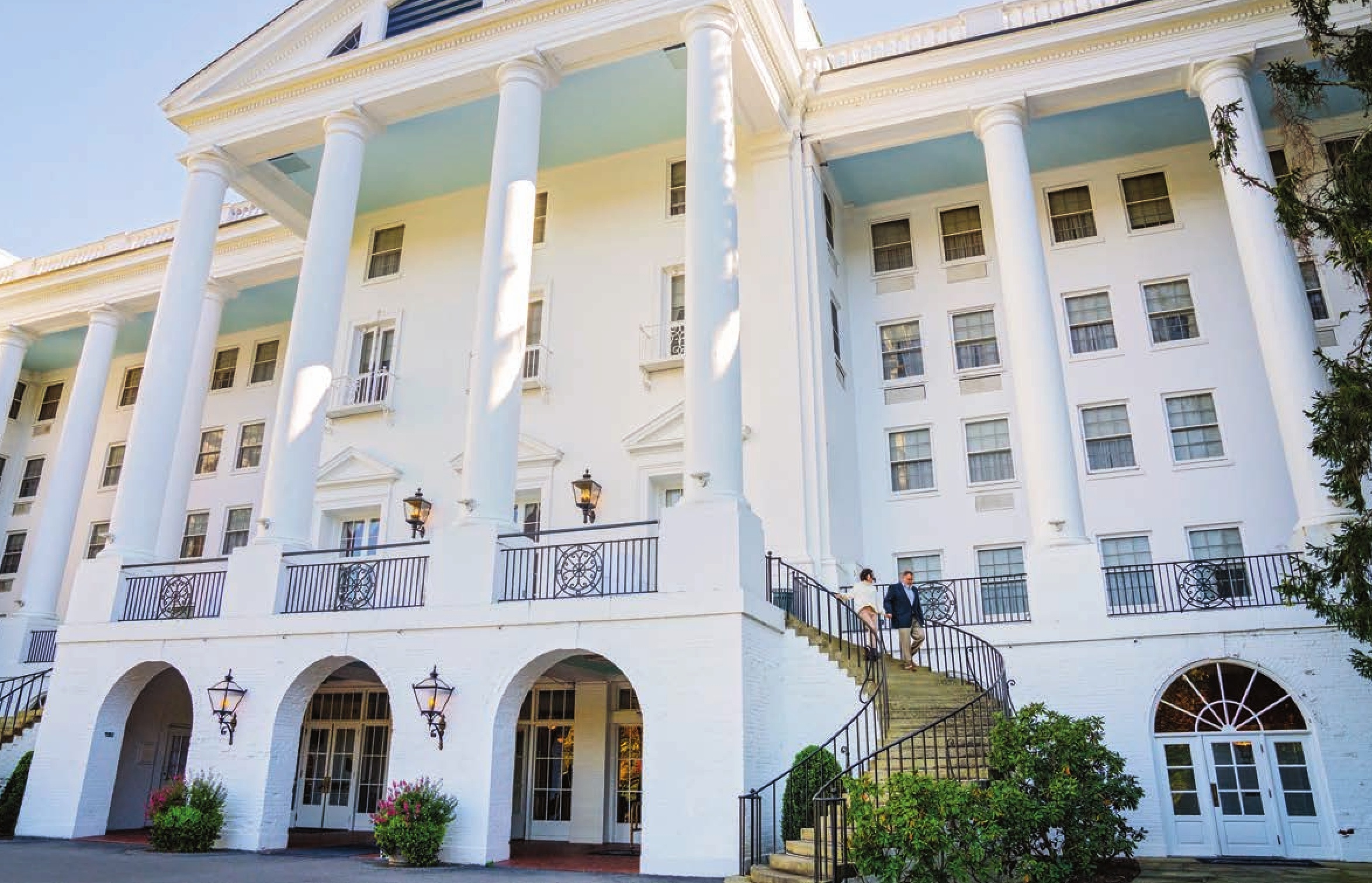 The bold white Greek Revival exterior of the Greenbrier hotel, with columns, a spiral staircase, and archways.