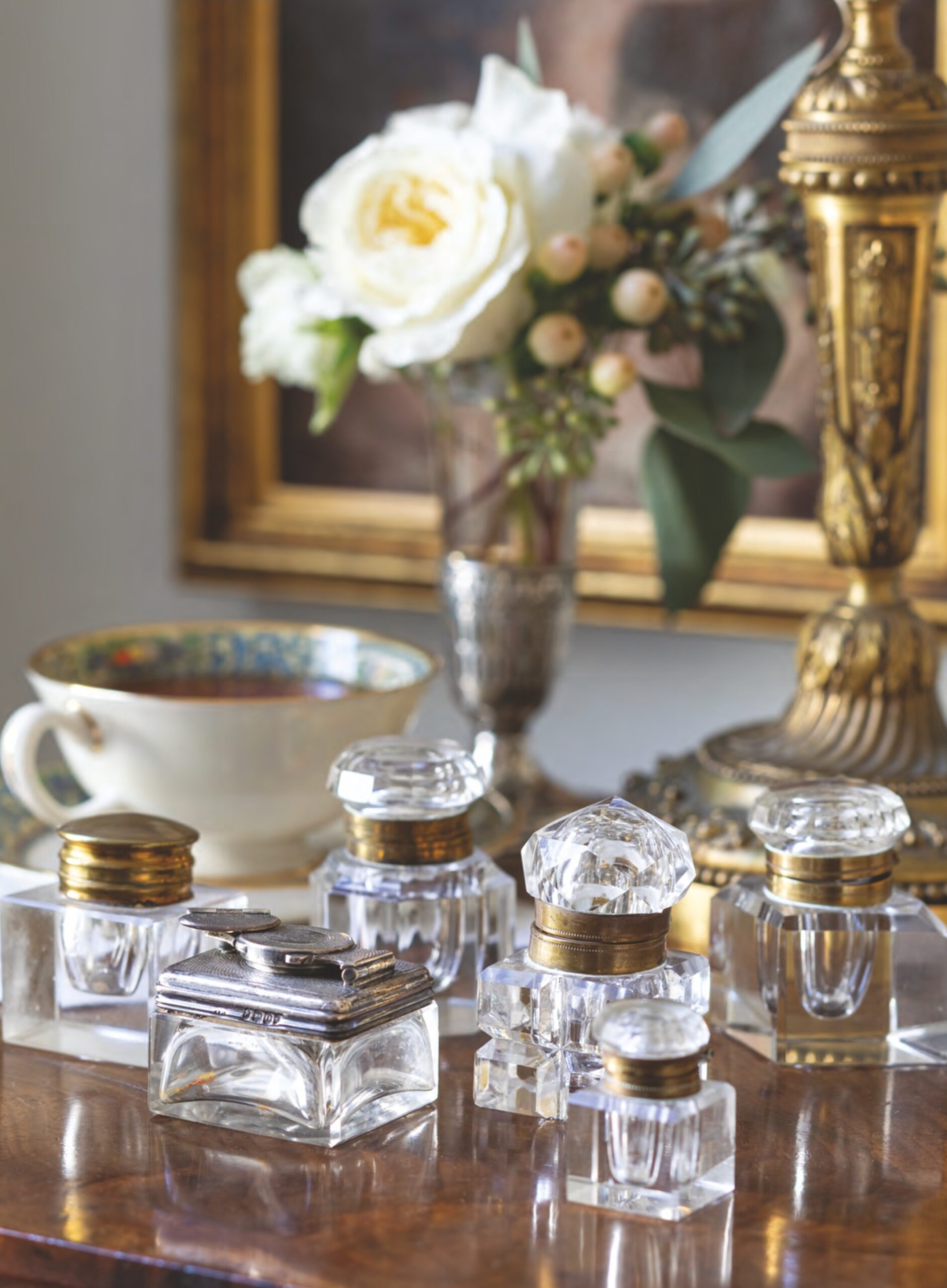 Antique and vintage inkwells arranged with a vase of flowers nearby.