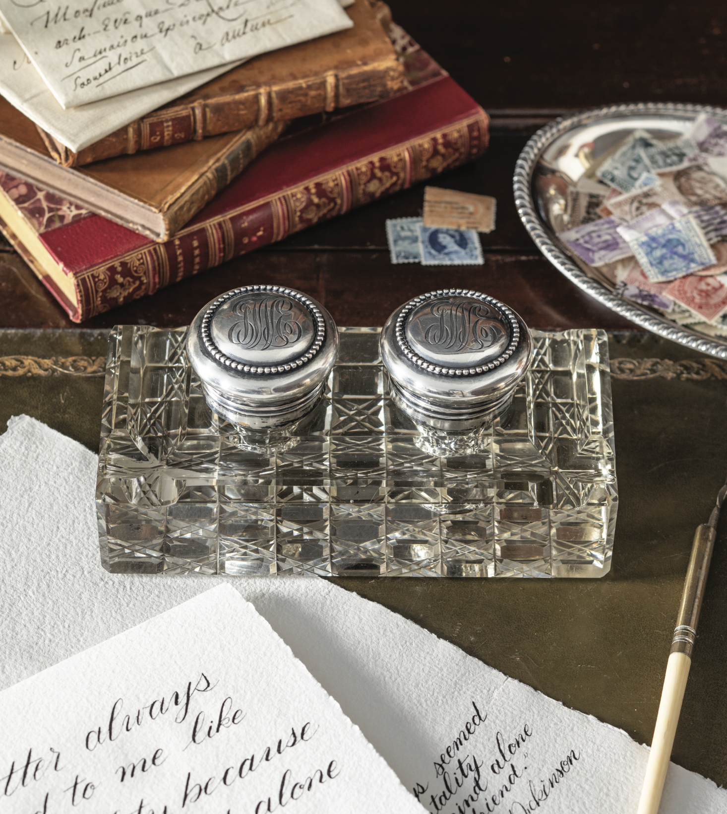 A double inkwell with monograms stamped into the lids near calligraphy pages.