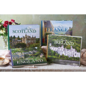 A collection of glossy travel books titled Scotland, England, Ireland, and France displayed on a table with a bouquet of flowers nearby.
