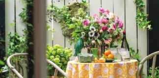 An alfresco outdoor table arranged in a garden with flowers and colorful decor.