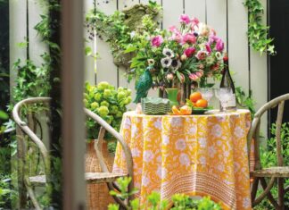 An alfresco outdoor table arranged in a garden with flowers and colorful decor.