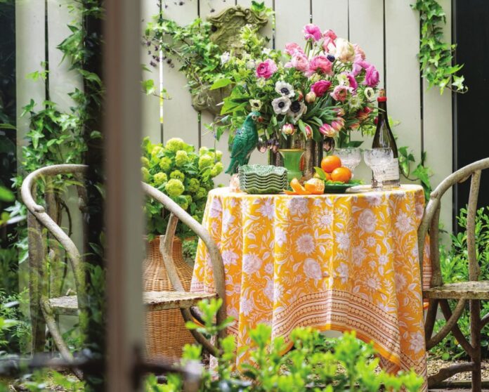 An alfresco outdoor table arranged in a garden with flowers and colorful decor.