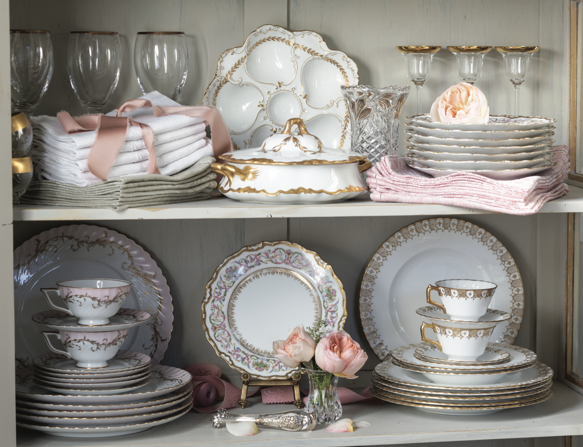 Ornate dishware and glassware in a china hutch, including goblets, tea cups, plates, a casserole dish, and an oyster plate.