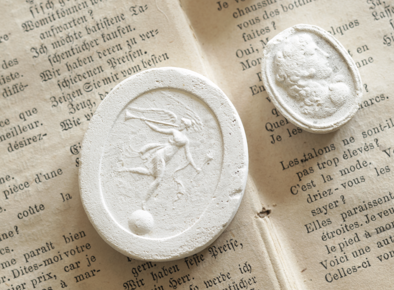 Two plaster intaglios, one with a trumpet player, and one of a side profile portrait.