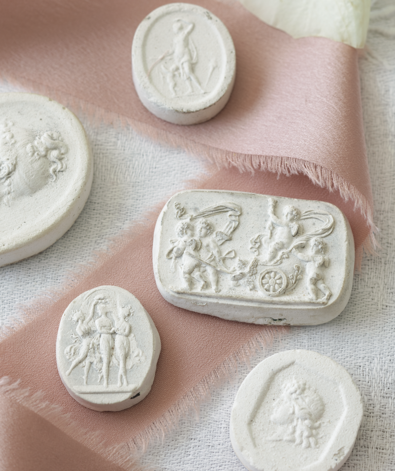 Plaster intaglios layered over pink ribbon featuring classical scenes.