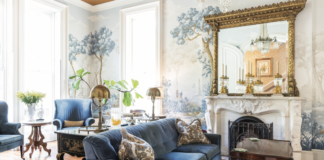 The luxurious antique interior of Savannah's Hamilton-Turner Inn, featuring a sofa with blue upholstery, a wallpaper mural, a fireplace, and a gilfed mirror.