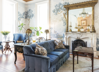 The luxurious antique interior of Savannah's Hamilton-Turner Inn, featuring a sofa with blue upholstery, a wallpaper mural, a fireplace, and a gilfed mirror.