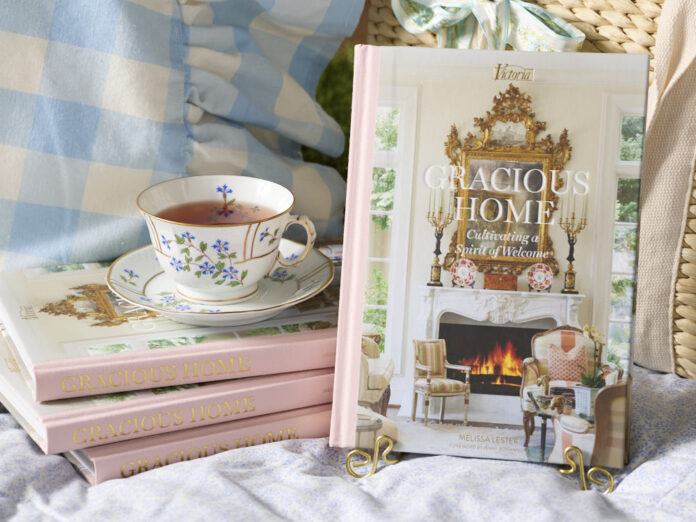 A stack of books with a pink spine are crowned with a porcelain cup of tea, beside which the cover of Gracious Home is displayed.