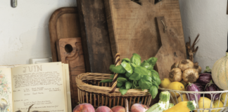 A counter in a French Country kitchen with cutting boards, a cookbook, and baskets of fresh vegetables.