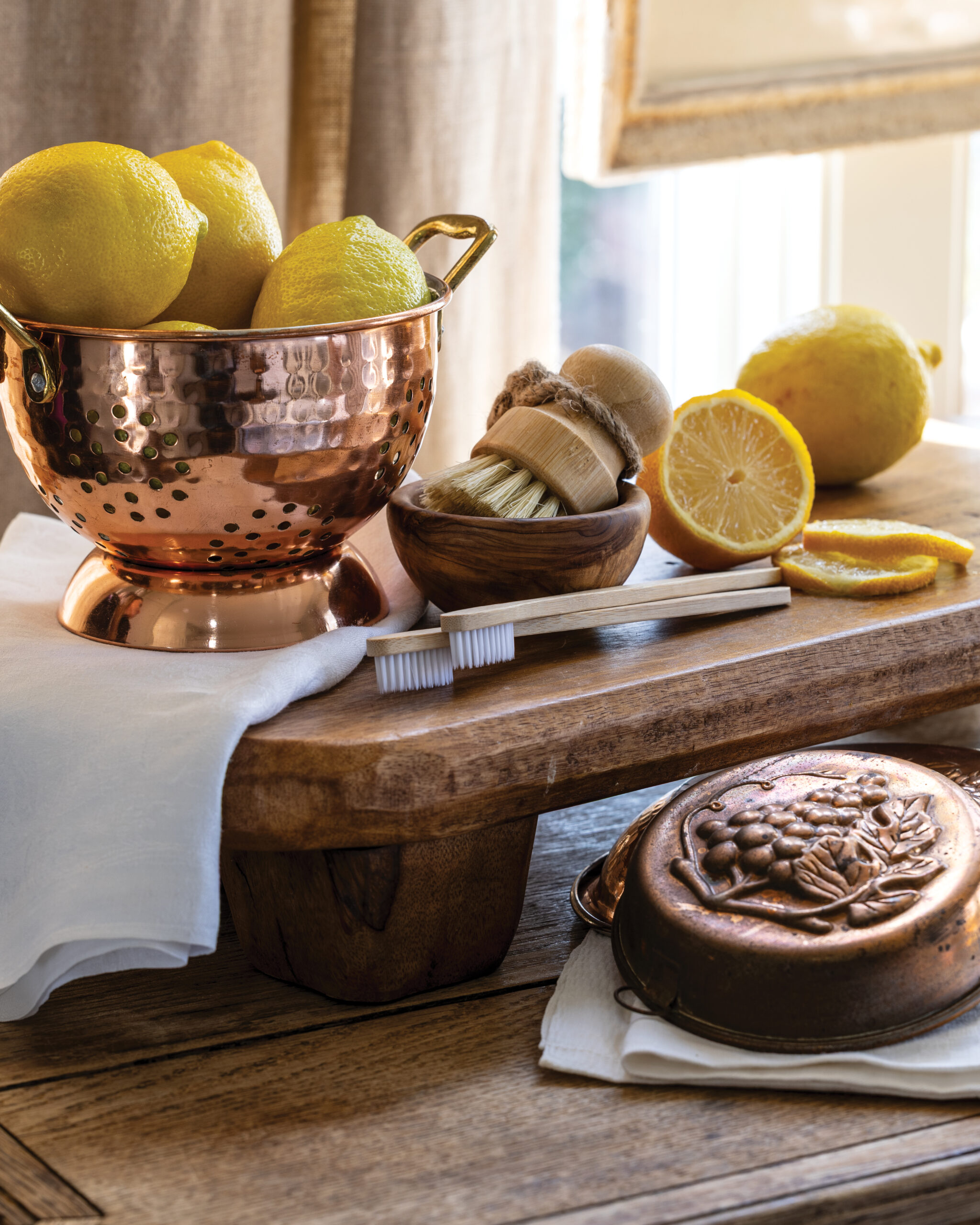 Copper colander with lemons next to brushes used to clean copper