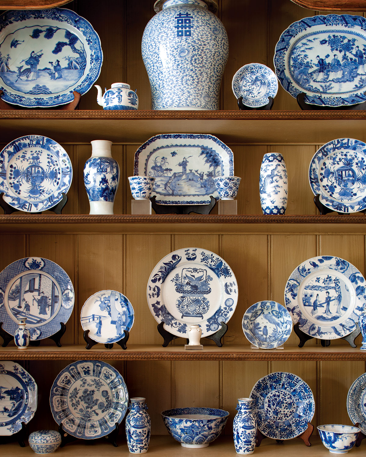 Blue-and-white porcelain plates, bowls, and vases arranged on wooden display shelves, featuring intricate floral and scenic patterns in a traditional chinoiserie style.