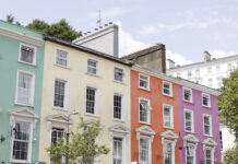 Colorful pastel row houses in Cobh, Ireland—painted mint green, pale yellow, coral orange, and pink—line a sunny street with café storefronts below and white-trimmed windows above.