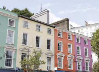 Colorful pastel row houses in Cobh, Ireland—painted mint green, pale yellow, coral orange, and pink—line a sunny street with café storefronts below and white-trimmed windows above.