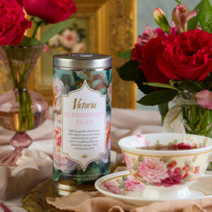 Floral-patterned tin of Victoria Elderberry Élan tea beside a floral teacup and pink roses on a table setting