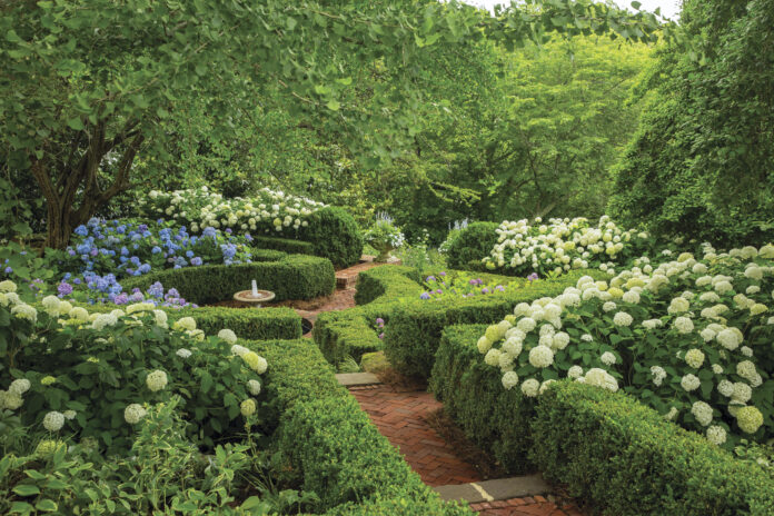 web featured garden with brick walking path and hydrangeas and bubbling fountain in the center of hedges