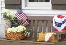 Letters fromVictoria: Defining a Nation brown porch bench with basket of flowers, picnic basket, and American flah decor