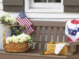brown porch bench with basket of flowers, picnic basket, and American flah decor
