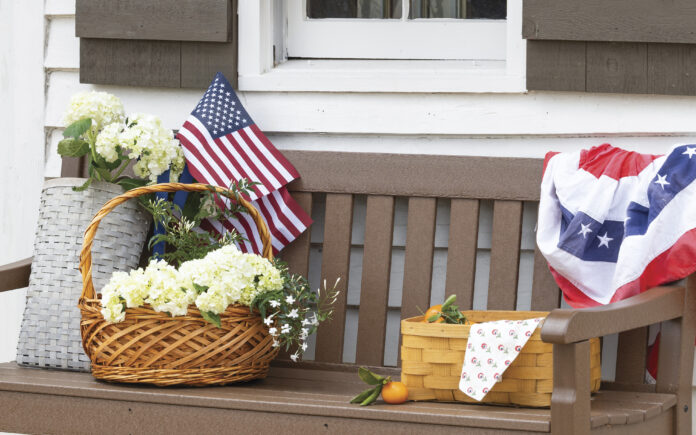 web featured_1 brown porch bench with basket of flowers, picnic basket, and American flah decor